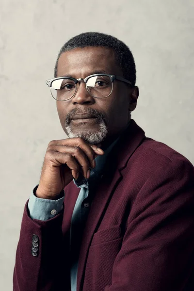 Portrait of pensive african american man in trendy eyeglasses and burgundy jacket — Stock Photo
