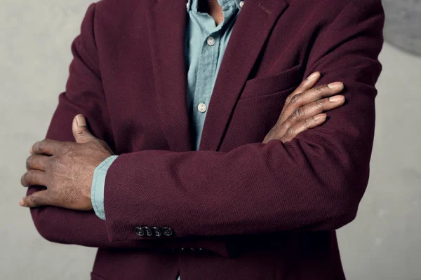 Обрізаний вид на стильного афроамериканця з схрещеними руками в бордовому піджаку — стокове фото