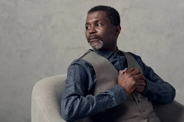 Portrait of serious african american man in waistcoat sitting in armchair — Stock Photo
