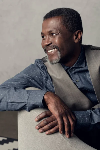 Portrait of handsome smiling middle aged african american man in waistcoat sitting in armchair — Stock Photo