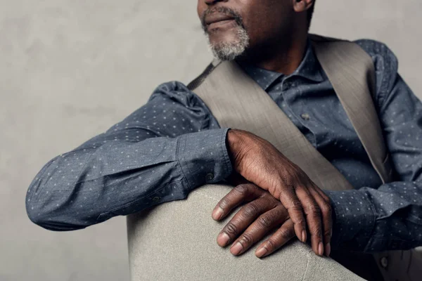 Vista cortada de homem americano africano elegante em colete sentado em poltrona — Fotografia de Stock