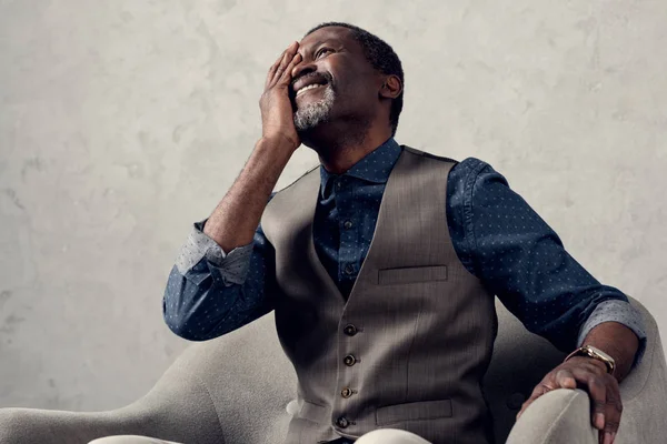Portrait of stylish laughing african american man in waistcoat sitting in armchair — Stock Photo