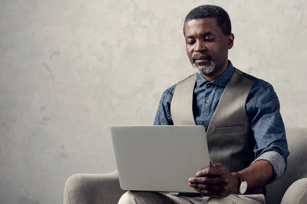 Fiducioso uomo d'affari africano americano con computer portatile seduto in poltrona — Foto stock
