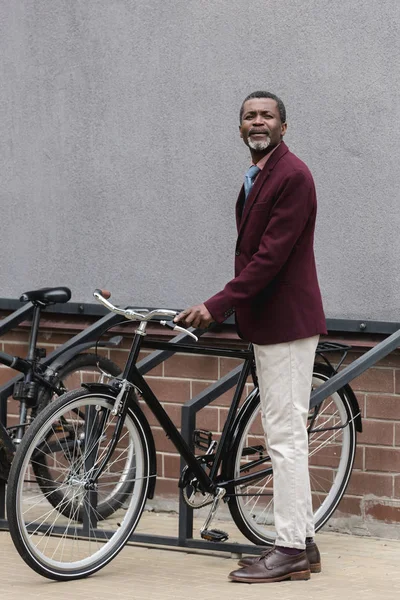Stylish african american businessman with bike on parking for bicycles — Stock Photo