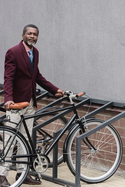 Homem de negócios americano africano maduro na moda com bicicleta no estacionamento para bicicletas — Fotografia de Stock