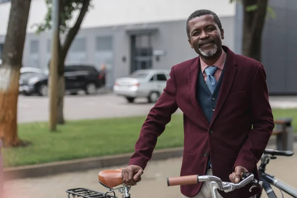 Sonriente afroamericano hombre con bicicleta en la ciudad - foto de stock