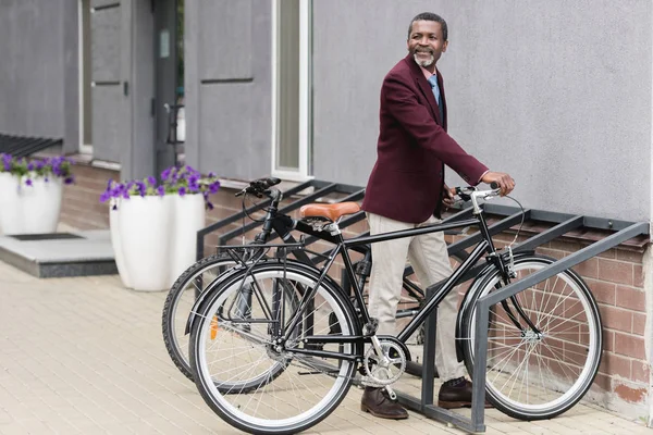 Hombre de negocios afroamericano de moda con bicicleta en el estacionamiento para bicicletas - foto de stock