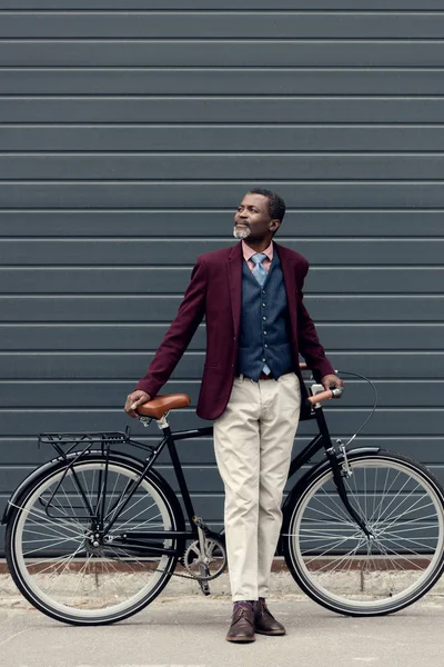 Stylish mature african american man in burgundy jacket posing near bicycle — Stock Photo