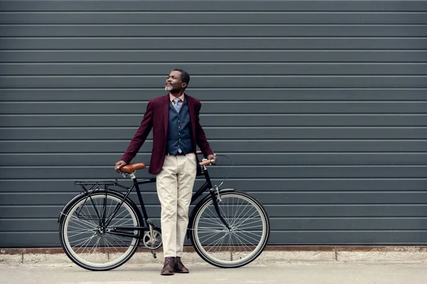 Modische afrikanisch-amerikanische Mann in trendiger Jacke posiert in der Nähe von Fahrrad — Stockfoto