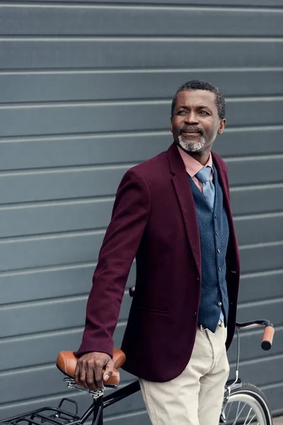 Stylish mature african american man in burgundy jacket posing near bicycle — Stock Photo