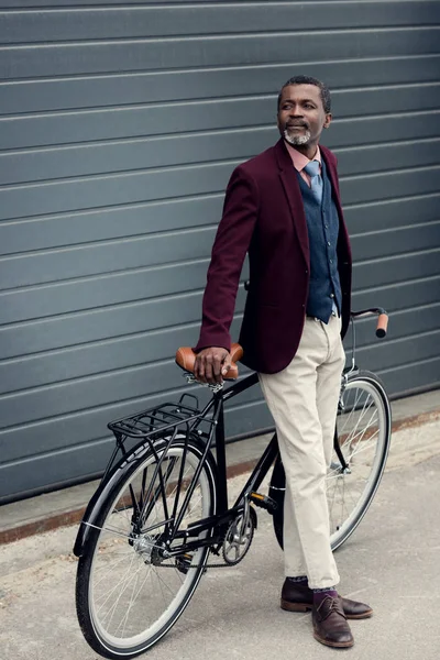 Bonito afro-americano homem em casaco de Borgonha posando perto de bicicleta — Fotografia de Stock