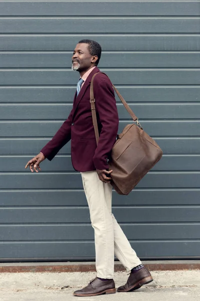 Stylish mature african american man posing in trendy burgundy jacket with leather bag — Stock Photo