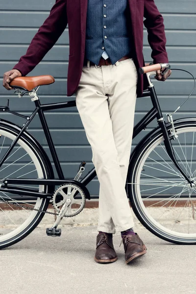 Низкий вид на секцию стильного человека в бордовом пиджаке, стоящего с велосипедом — стоковое фото