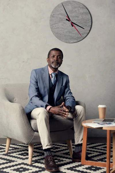 Confident african american businessman sitting at table with newspaper, coffee and laptop — Stock Photo