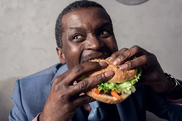 Hungry african american businessman eating hamburger — Stock Photo