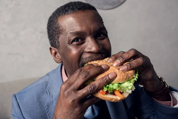 Hambriento africano americano hombre comer hamburguesa - foto de stock
