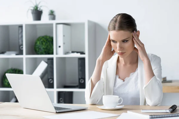 Jeune femme d'affaires surmenée avec maux de tête assis sur le lieu de travail au bureau et tenant la tête — Photo de stock