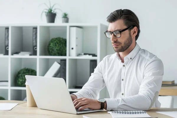 Joven empresario confiado que trabaja con el ordenador portátil en la oficina moderna — Stock Photo