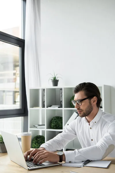 Joven empresario enfocado que trabaja con el ordenador portátil en la oficina moderna - foto de stock