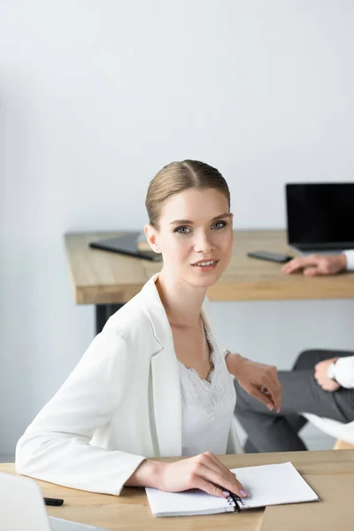 Schöne junge Geschäftsfrau sitzt am Arbeitsplatz mit Notizbuch — Stockfoto