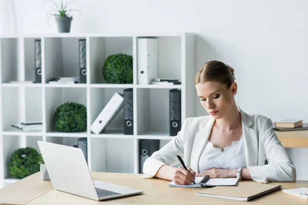 Зосереджена молода бізнес-леді робить нотатки під час роботи в офісі — стокове фото