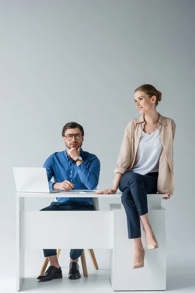 Handsome businessman sitting at workplace while his colleague sitting on his desk on white — Stock Photo
