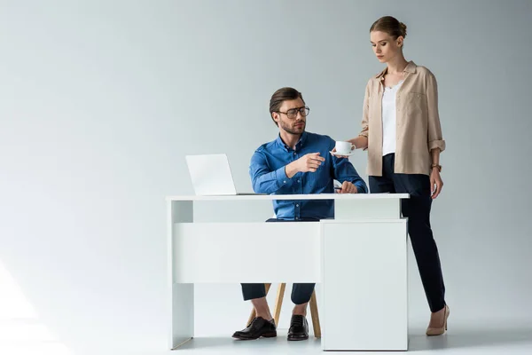 Atractivo joven secretaria pasando taza de café a jefe en blanco - foto de stock