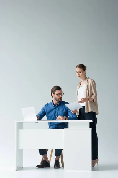 Красивий молодий бізнесмен сидить на робочому місці, а його колега передає йому документи на білому — стокове фото
