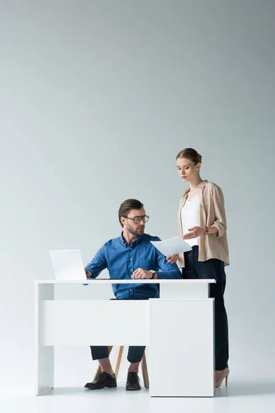 Bel giovane uomo d'affari seduto sul posto di lavoro mentre il suo collega gli passa i documenti su bianco — Foto stock