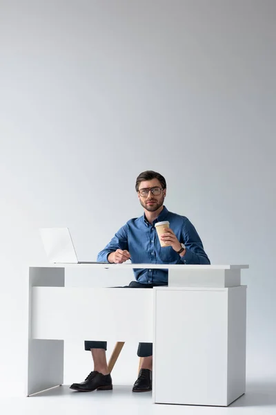 Handsome young businessman with laptop and coffee to go at workplace on white — Stock Photo