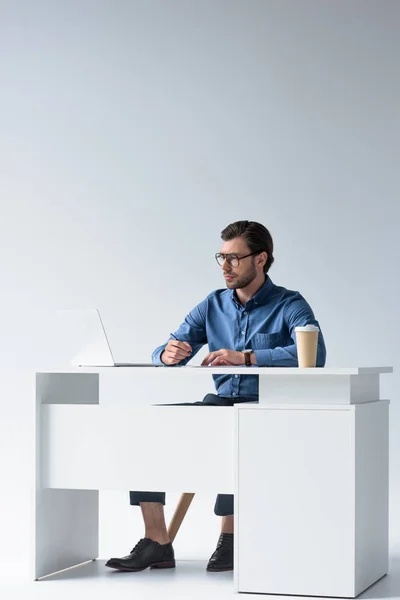 Joven hombre de negocios guapo usando el ordenador portátil en el lugar de trabajo en blanco — Stock Photo