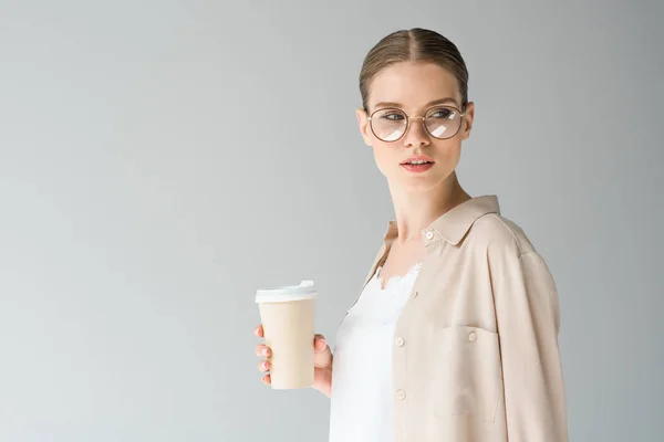 Mujer joven con estilo con taza de papel de café aislado en gris — Stock Photo