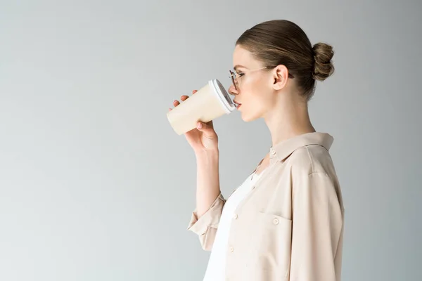 Seitenansicht der schönen jungen Frau, die Kaffee trinkt, um sich auf grau zu isolieren — Stockfoto