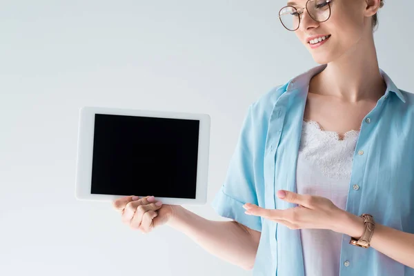 Улыбающаяся молодая женщина, показывающая планшет с чистым экраном, изолированным на сером — стоковое фото