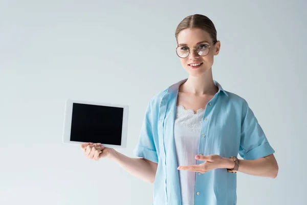 Glückliche junge Frau zeigt Tablet mit leerem Bildschirm isoliert auf grau — Stockfoto