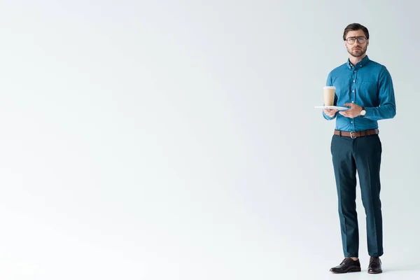 Handsome young man with paper cup of coffee and tablet on white — Stock Photo