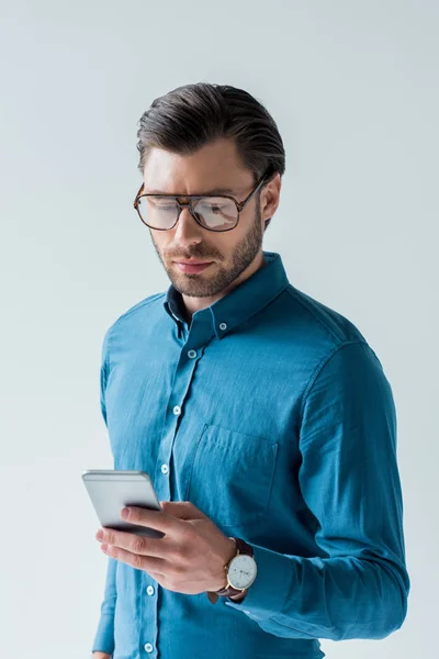 Joven confiado en gafas con estilo usando teléfono inteligente aislado en blanco - foto de stock