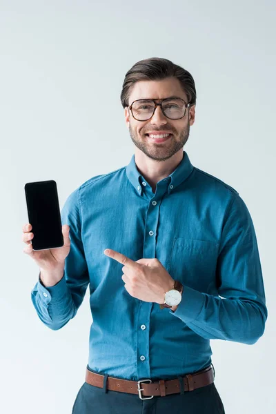 Happy young man holding smartphone and pointing at blank screen isolated on white — Stock Photo