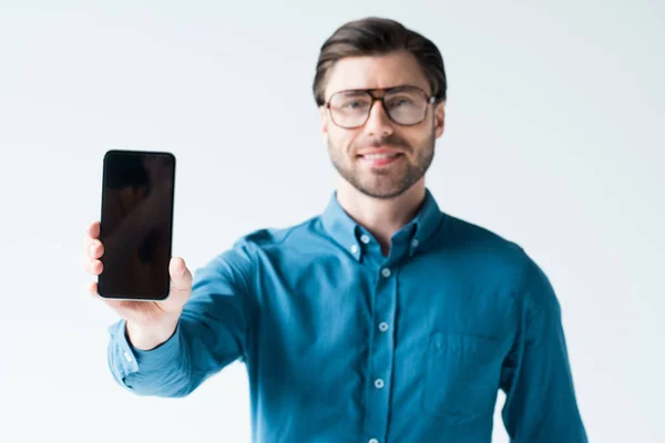 Усміхнений молодий чоловік тримає смартфон з порожнім екраном ізольовано на білому — стокове фото