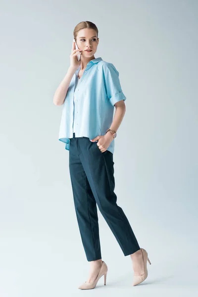 Attractive young woman in blue shirt talking by phone on grey — Stock Photo