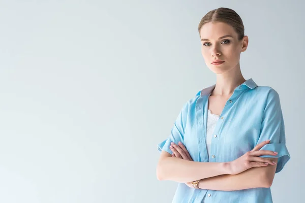 Schöne junge Frau in blauem Hemd mit verschränkten Armen vereinzelt auf grau — Stockfoto
