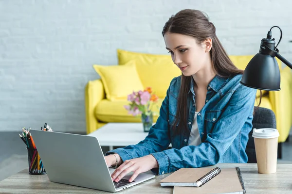 Chica sonriente usando el ordenador portátil mientras estudia en casa - foto de stock