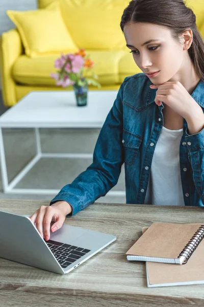 Menina focada usando laptop enquanto sentado na mesa de madeira em casa — Fotografia de Stock