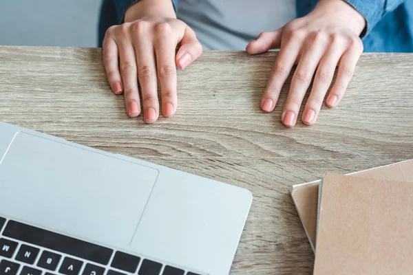 Close-up partial view of female hands on wooden table with laptop and notebooks — Stock Photo