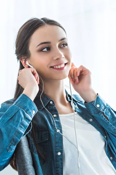 Hermosa sonrisa adolescente escuchando música en los auriculares y mirando hacia otro lado - foto de stock