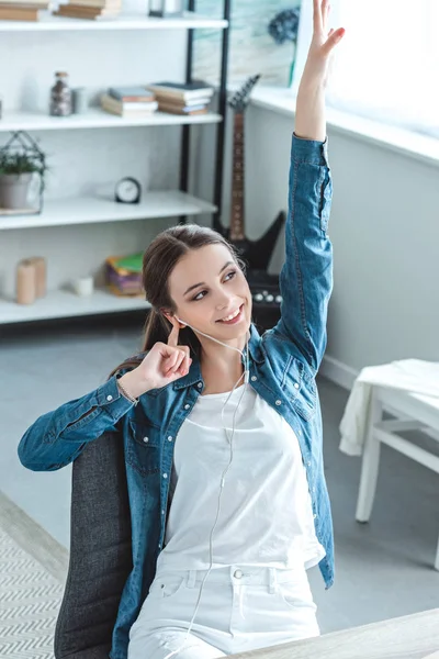 High angle view of happy teenage girl listening music in earphones and raising hand at home — Stock Photo