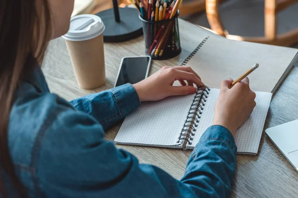 Plan recadré de fille prenant des notes dans un carnet tout en étudiant à la maison — Photo de stock