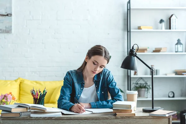 Концентрированная девочка-подросток пишет и учится на рабочем столе дома — стоковое фото