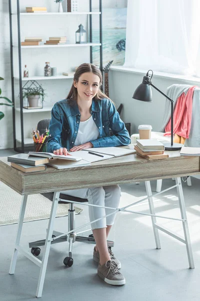 Beautiful teenage girl smiling at camera while sitting at desk and studying at home — Stock Photo