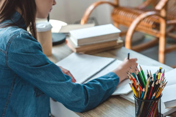 Colpo ritagliato di ragazza adolescente che scrive nel taccuino mentre studia a casa — Foto stock